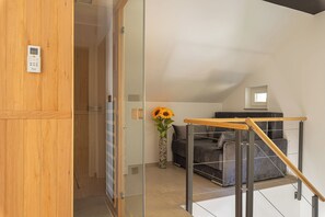 A modern room with a glass door, a wooden panel wall, a sofa, a small table, and a vase with sunflowers. - Wellness Resort Trebnje (Trebnje)