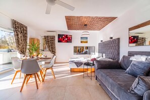 A modern living room with a sofa, a dining area with chairs and a table, a large mirror, and a ceiling fan. - Wellness Resort Trebnje (Trebnje)