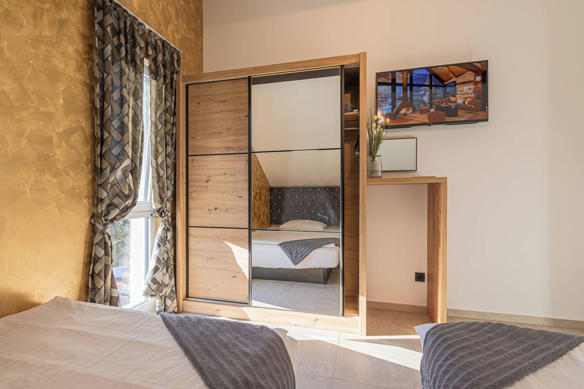 A bedroom with a large mirror, a bed, a wardrobe, and a television on the wall.