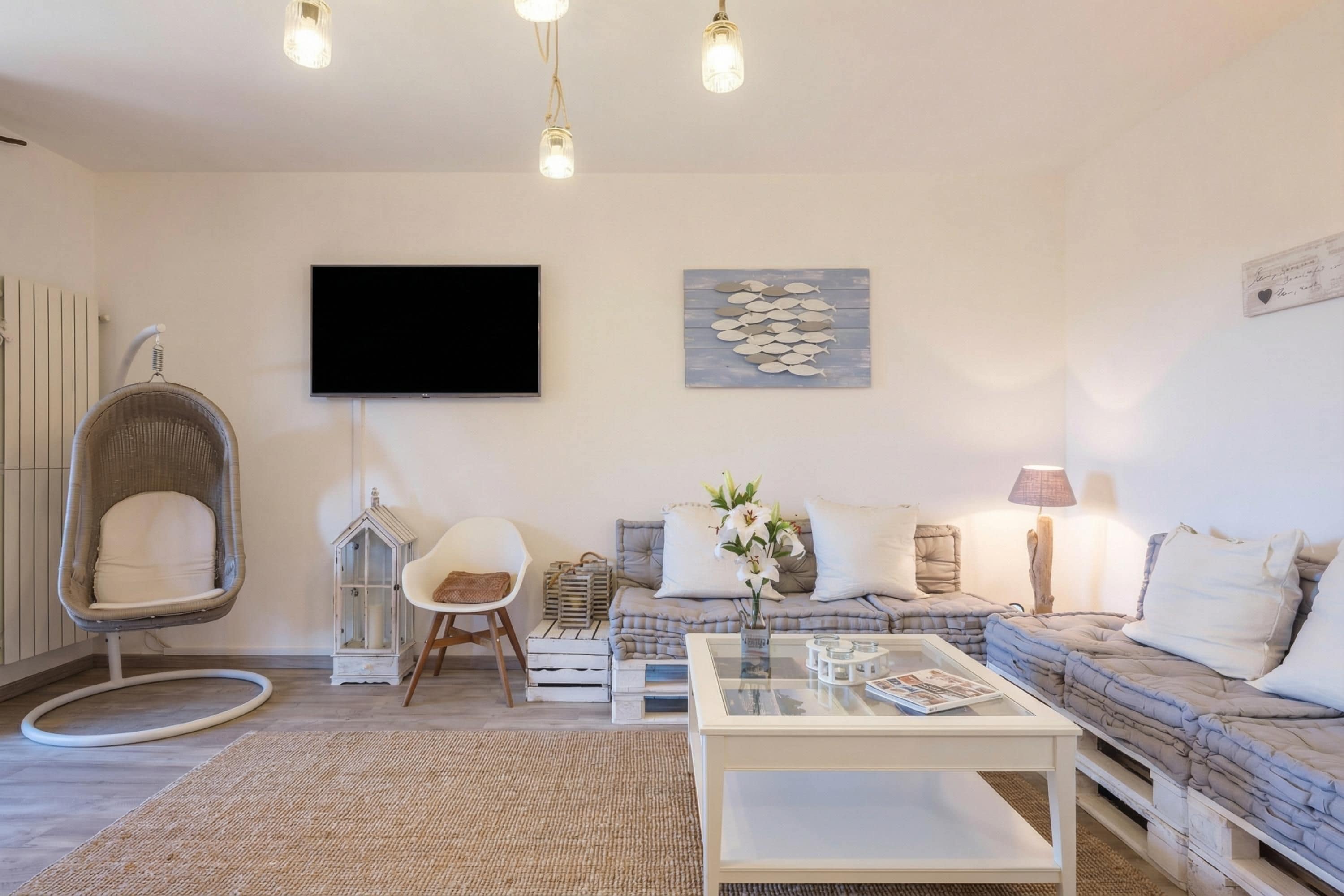 Una sala de estar moderna con un sofá, una mesa de centro de cristal, una silla colgante, un televisor de pantalla plana y un adorno en la pared.