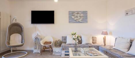 Una sala de estar moderna con un sofá, una mesa de centro de cristal, una silla colgante, un televisor de pantalla plana y un adorno en la pared.