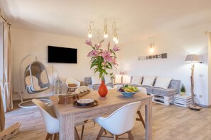 A modern living room with a dining table, chairs, a hanging chair, a sofa, a TV, and a vase with flowers.