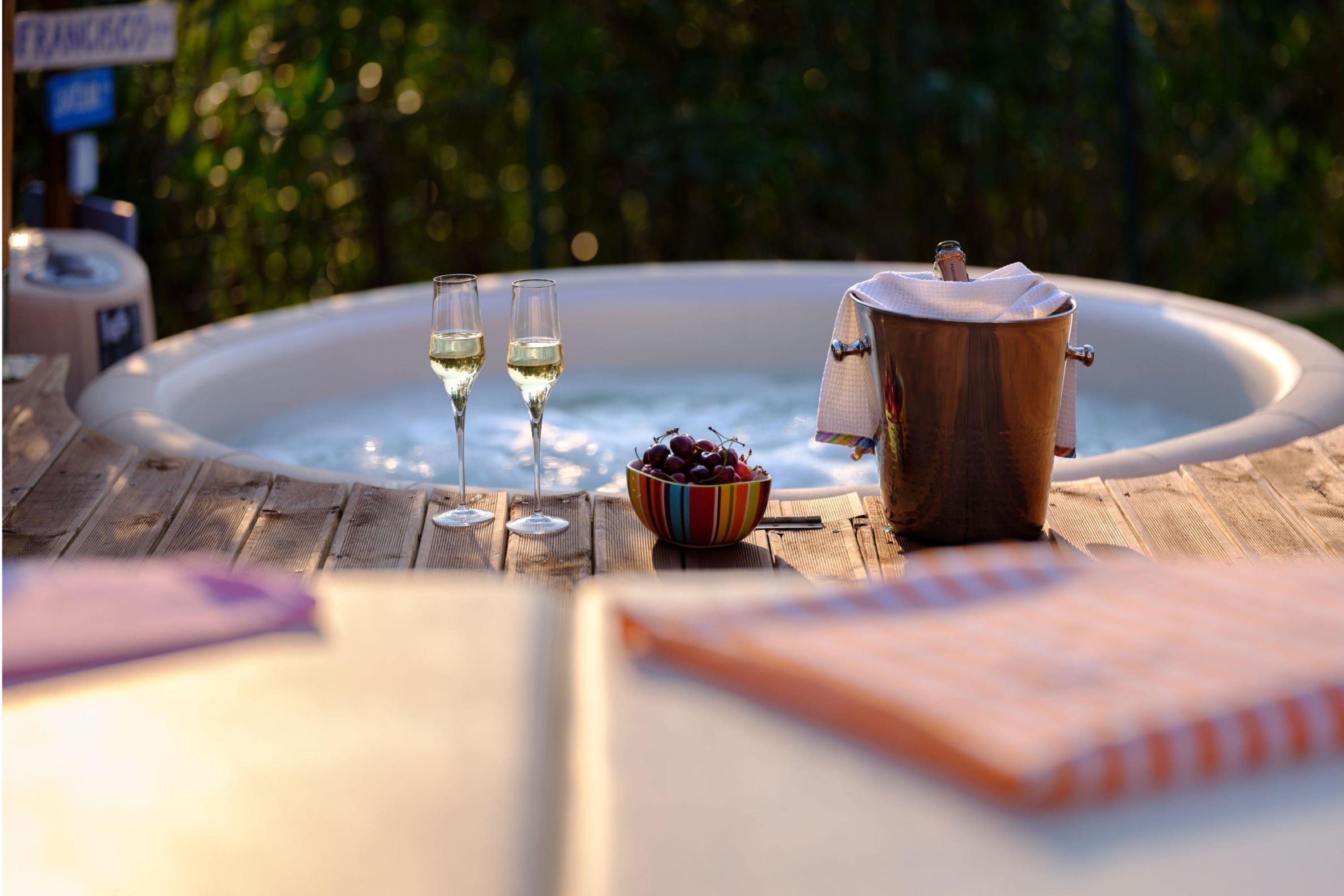 Un bain à remous, deux verres de vin blanc, un saladier de cerises et un seau de champagne, le tout sur une terrasse en bois.