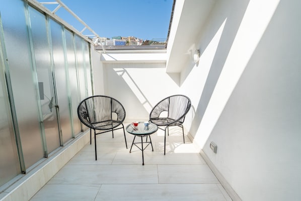 A small balcony with two chairs and a table, a glass door, and a white wall.