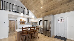 Une cuisine moderne avec un plafond en bois, des appareils électroménagers en acier inoxydable et un coin repas doté de chaises en bois.