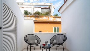 Eine kleine Außenveranda mit zwei Stühlen, einem Tisch und einer weißen Tür, mit Blick auf ein Gebäude mit einem Balkon.