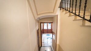 Ein Flur mit Marmorboden, einer Holztür am Ende und einer Treppe mit schwarzer Geländer.