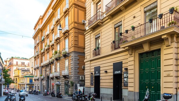 A cobblestone street lined with multi-story buildings, some with balconies and shopfronts. - Colonna Apartment 4 by Wonderful Italy (Napoli)