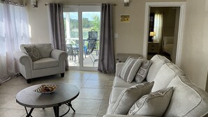 Ein Wohnzimmer mit einer Couch, einem runden Tisch mit einer Obstschale und einer Glastür, die zu einem Außenbereich mit Laufband führt.