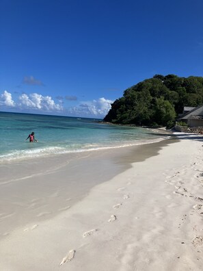 A beach with clear turquoise water, a sandy shore, and a forested hill in the background. - Caribbean Sun, Sand, Sea-Relax In The Peace and Quiet of Tropical Escape Villa! (Wilikies)