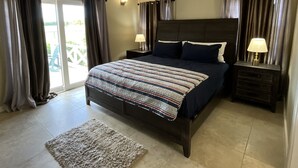 Ein Schlafzimmer mit Bett, Deckenventilator, Nachttisch mit Lampe und Fenster mit Vorhängen.