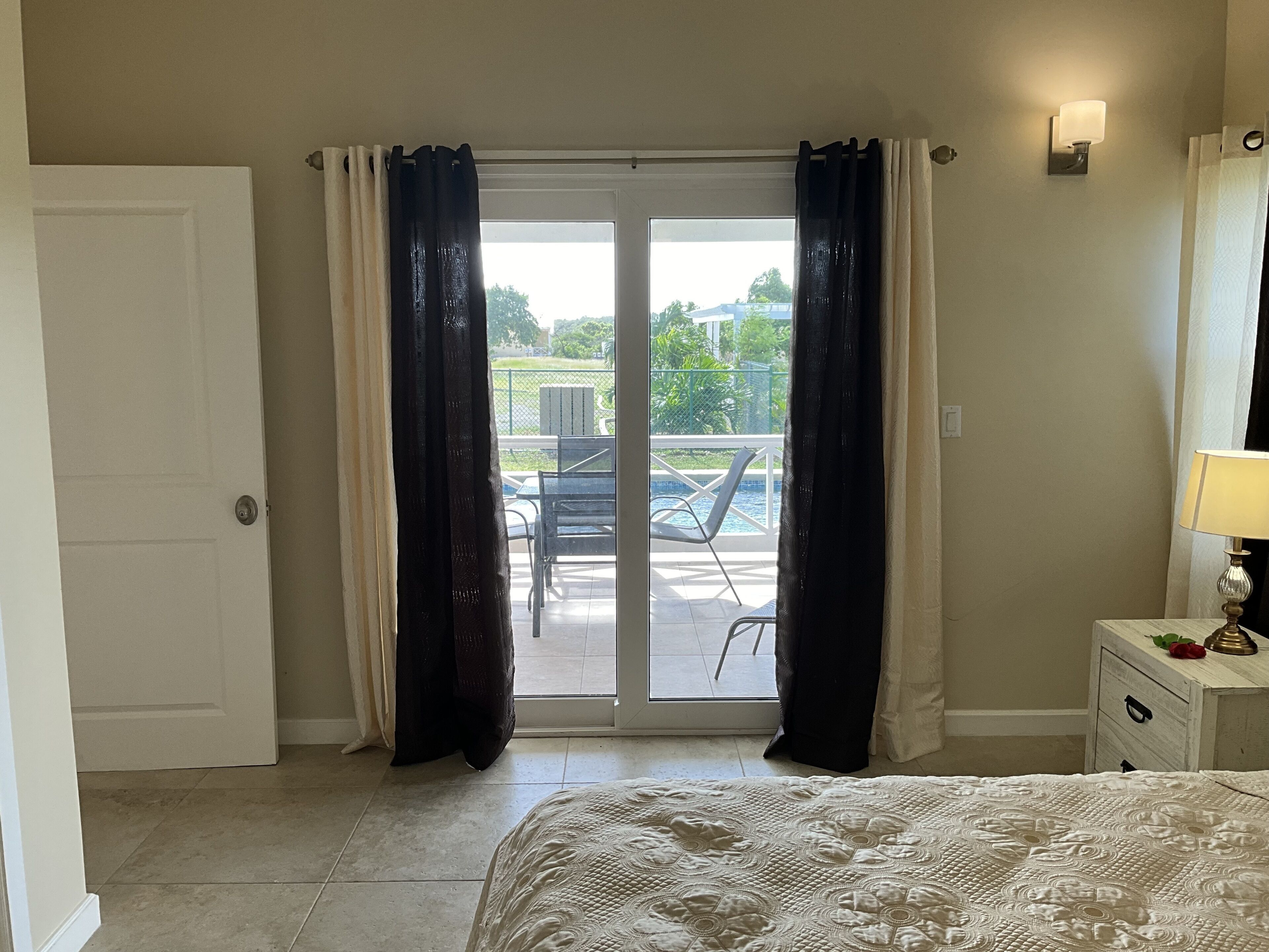 A hotel room with a bed, a nightstand, a lamp, and a view of an outdoor pool area.