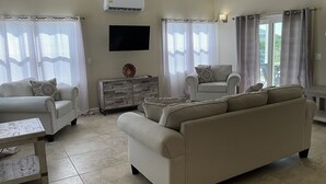 Ein Wohnzimmer mit einer Couch, Sesseln, einem Fernseher und einem Holzschrank.