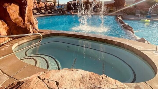 Un espace piscine agrémenté d’une formation rocheuse naturelle au-dessus, d’un jacuzzi et offrant une vue dégagée sur le paysage environnant.