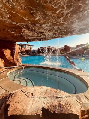 Ein Poolbereich mit einer natürlichen Felsformation darüber, einem Whirlpool und freiem Blick auf die umliegende Landschaft.