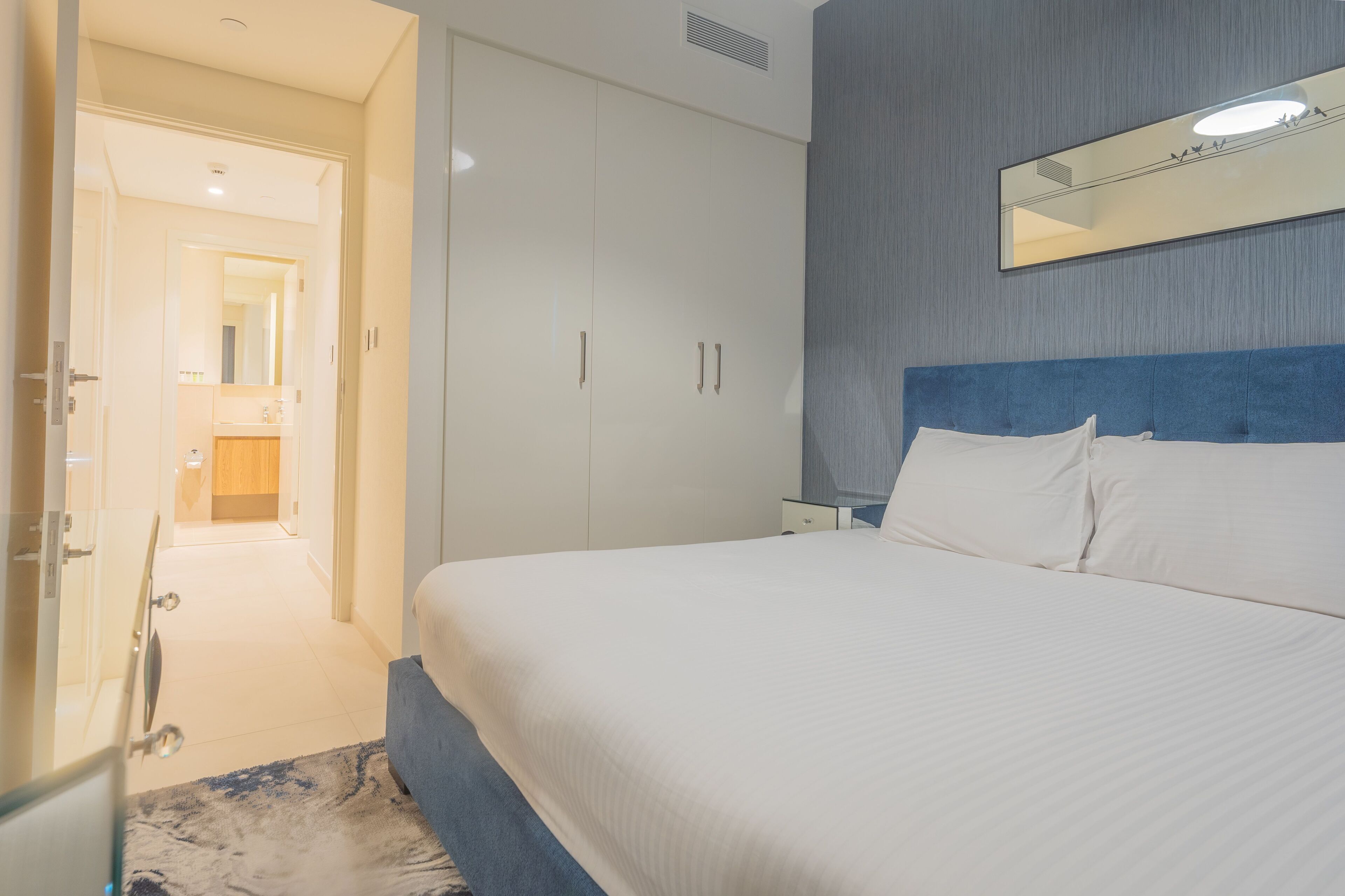 Une chambre d’hôtel avec un grand lit, une armoire, un miroir et une salle de bain visible à travers une porte ouverte.
