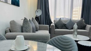 A modern living room with a sofa set, a dining table with plates and cutlery, and a large window with curtains. - WAAFI CITY CENTER RESIDENCE (Djibouti)