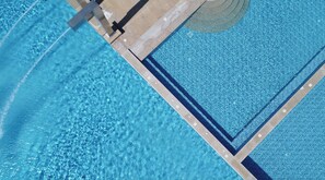 Vista aérea de una piscina con agua azul cristalina, carriles delimitados y una zona de solárium con baldosas.