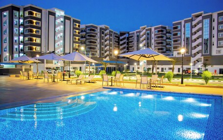 A swimming pool with lounge chairs and umbrellas, surrounded by multi-story buildings with balconies.