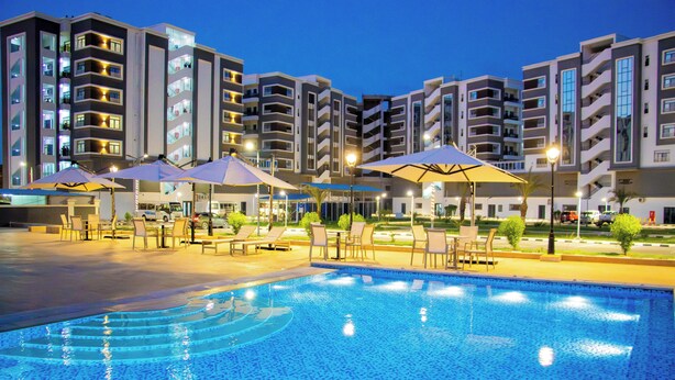 A swimming pool with lounge chairs and umbrellas, surrounded by multi-story buildings with balconies. - WAAFI CITY CENTER RESIDENCE (Djibouti)