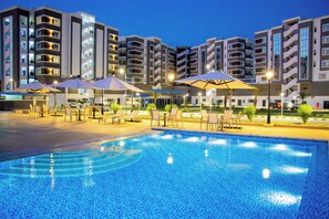 A swimming pool with lounge chairs and umbrellas, surrounded by multi-story buildings with balconies. - WAAFI CITY CENTER RESIDENCE (Djibouti)