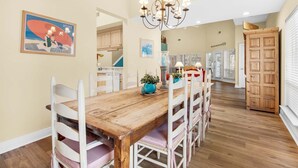 Un comedor con mesa de madera y sillas blancas, una araña y obras de arte en la pared.