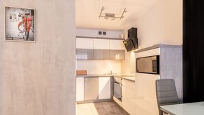 Cocina compacta con armarios blancos, microondas y un pequeño comedor con una silla.