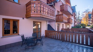 Un edificio con balcones de madera, un patio con mesa y sillas, y una cerca de madera.
