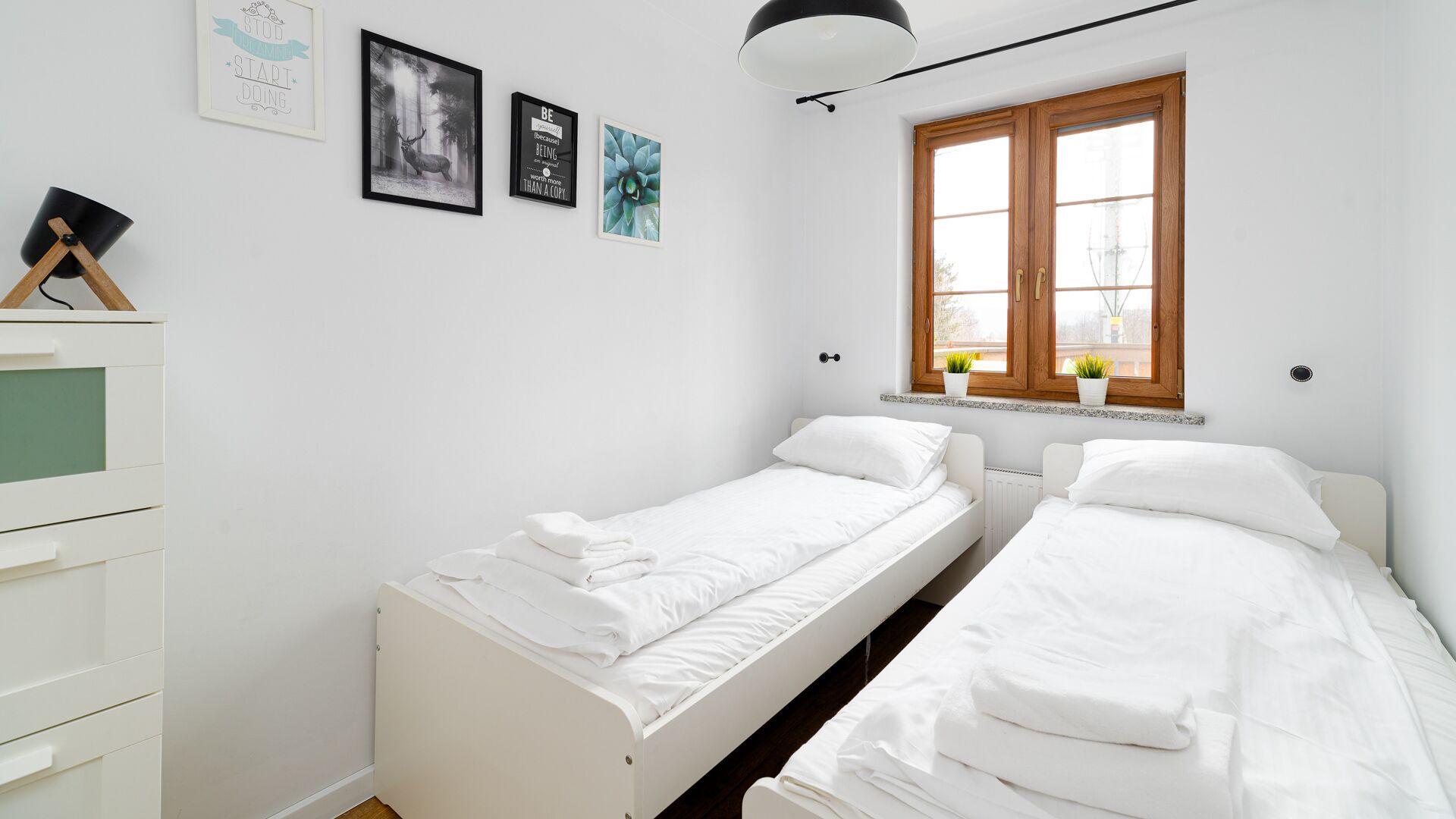 A small, clean room with two single beds, a dresser, and a window with wooden shutters.