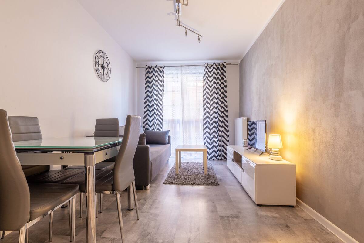 A modern living room with a dining area, a sofa, a coffee table, and a TV on a stand.