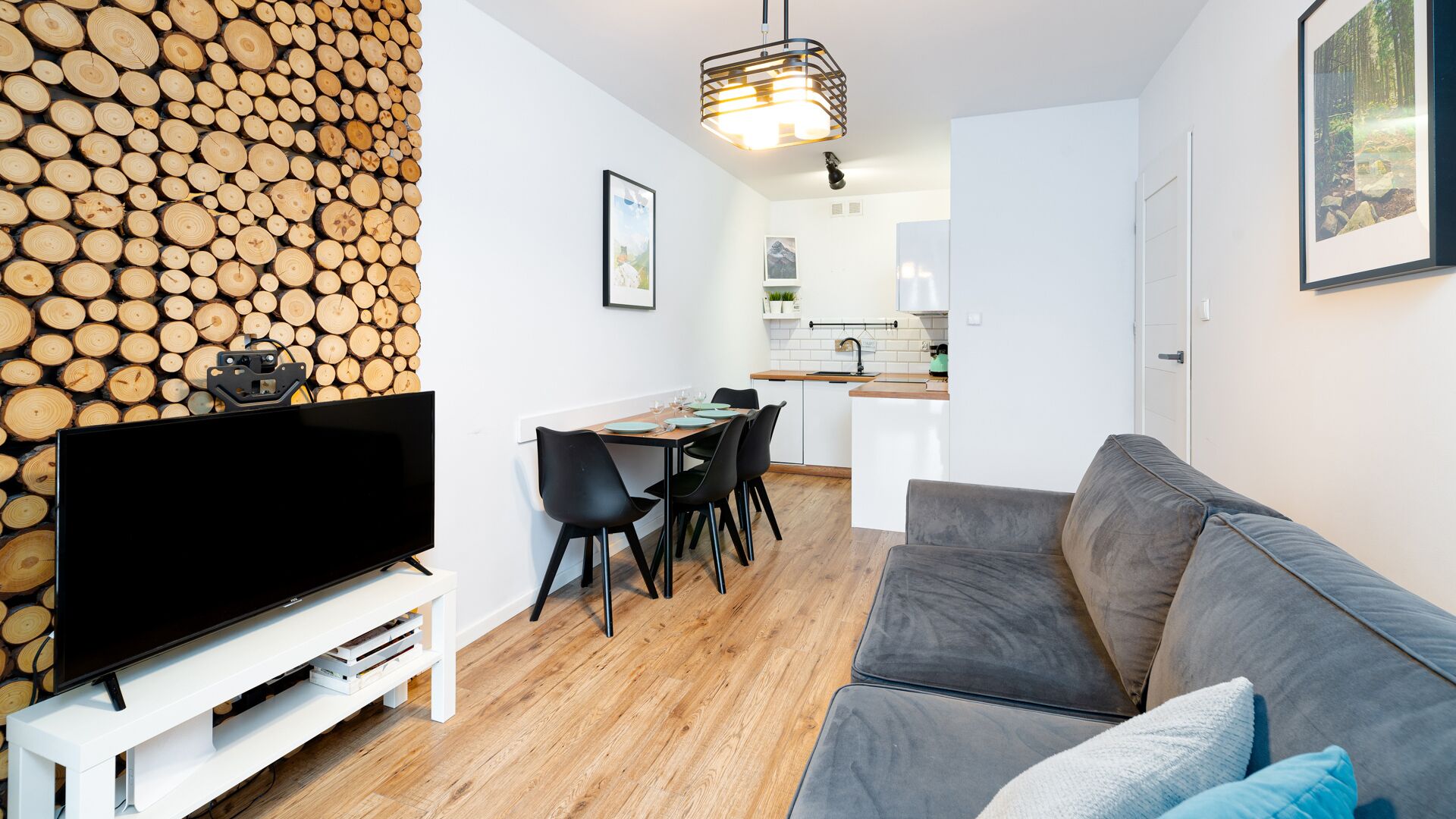 A modern living room with a grey sofa, a flat-screen TV on a white stand, and a dining area with a table and chairs.