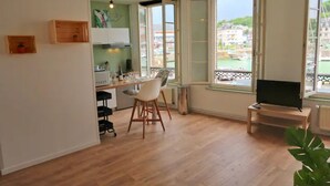 A spacious living area with a dining table, chairs, a television on a stand, and large windows offering a view of the outside. - La Jungle - Vue Directe et Magnifique sur le Port (Saint-Valery-en-Caux)