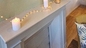 A cozy living room with a white fireplace mantel, a green accent wall, and a small table with candles and decorative items. - La Jungle - Vue Directe et Magnifique sur le Port (Saint-Valery-en-Caux)