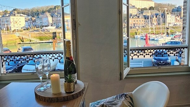 A room with a view of a marina and buildings, a wooden table with a candle and glasses, and a white chair. - La Jungle - Vue Directe et Magnifique sur le Port (Saint-Valery-en-Caux)