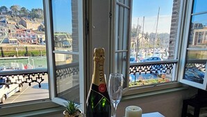 A bottle of Moët & Chandon champagne on a wooden coaster, a glass, and a candle on a table by a window with a marina view. - La Jungle - Vue Directe et Magnifique sur le Port (Saint-Valery-en-Caux)