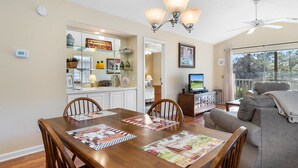 A dining area with a wooden table, chairs, and a chandelier. There is a television on a stand and a sofa in the background. - TB 19H Par tee Updated and spacious three bedroom condo in True Blue (Pawleys Island)