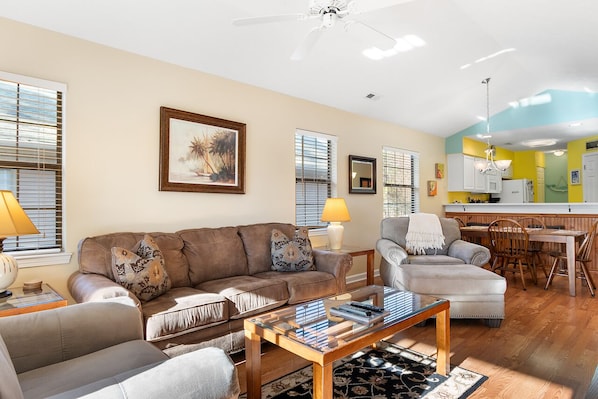 Relax in this open-plan living space featuring a sofa, armchair, and dining area with a wooden table.