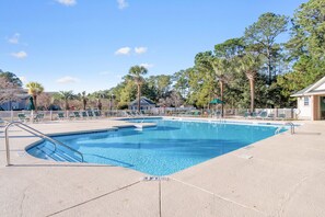 Relax by the pool surrounded by lush trees and a building with a green roof.