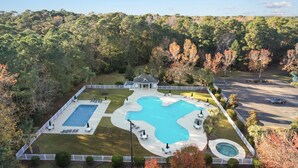 A large, rectangular swimming pool with a unique wavy design, surrounded by a white fence and multiple lounge chairs. - TB 19H Par tee Updated and spacious three bedroom condo in True Blue (Pawleys Island)