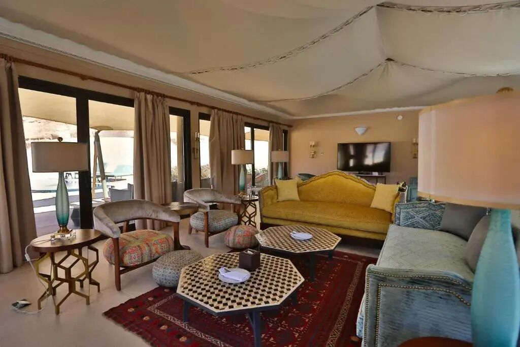 A hotel room with a sofa, armchairs, a television, and a patterned rug.