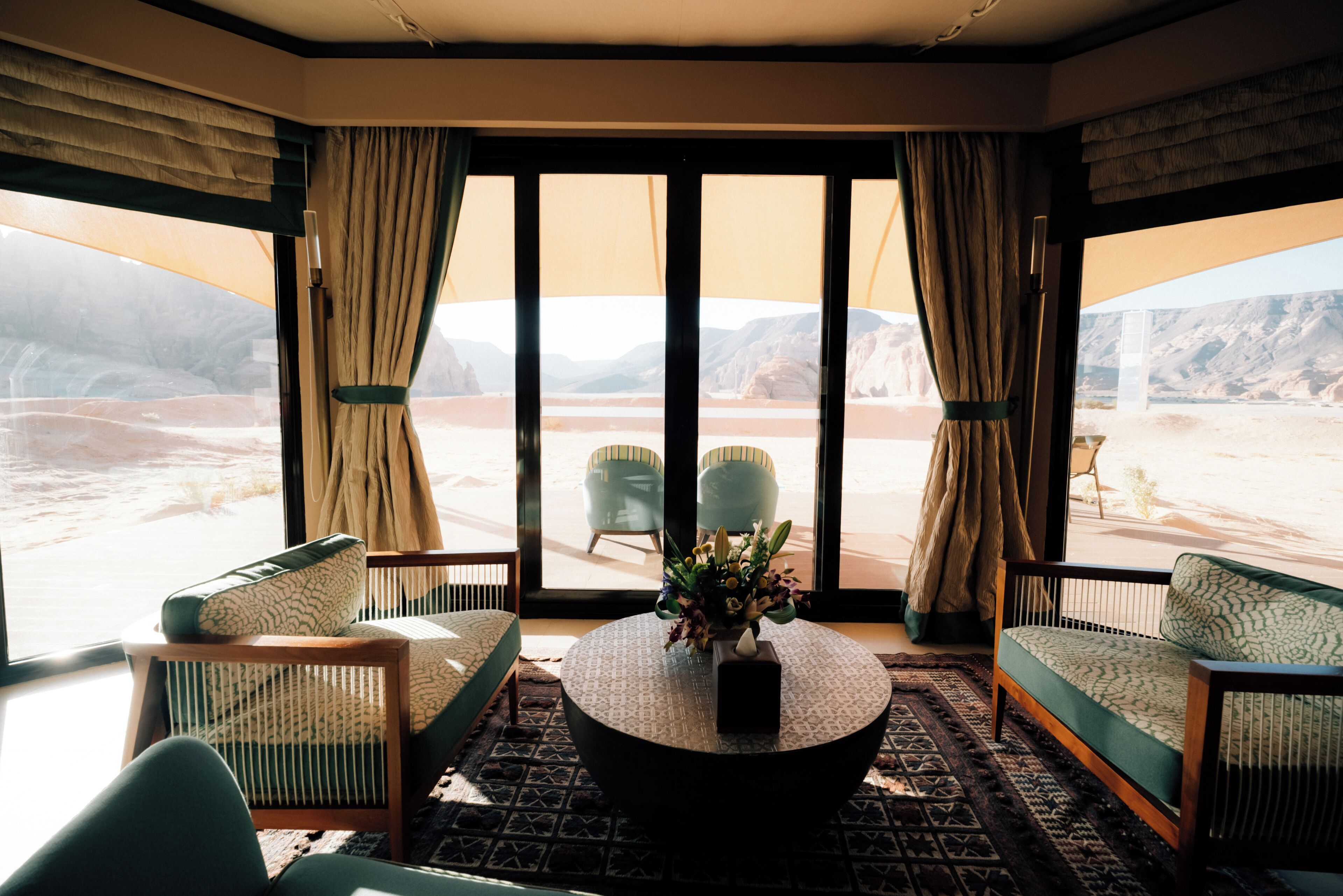 A room with a large window, two chairs, a sofa, and a coffee table with a vase of flowers.