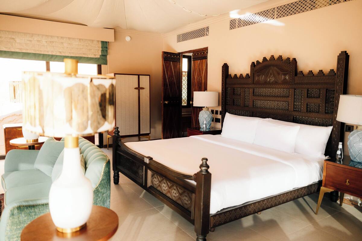 A hotel room with a large bed, a sitting area with a sofa, a wardrobe, and a mirror.