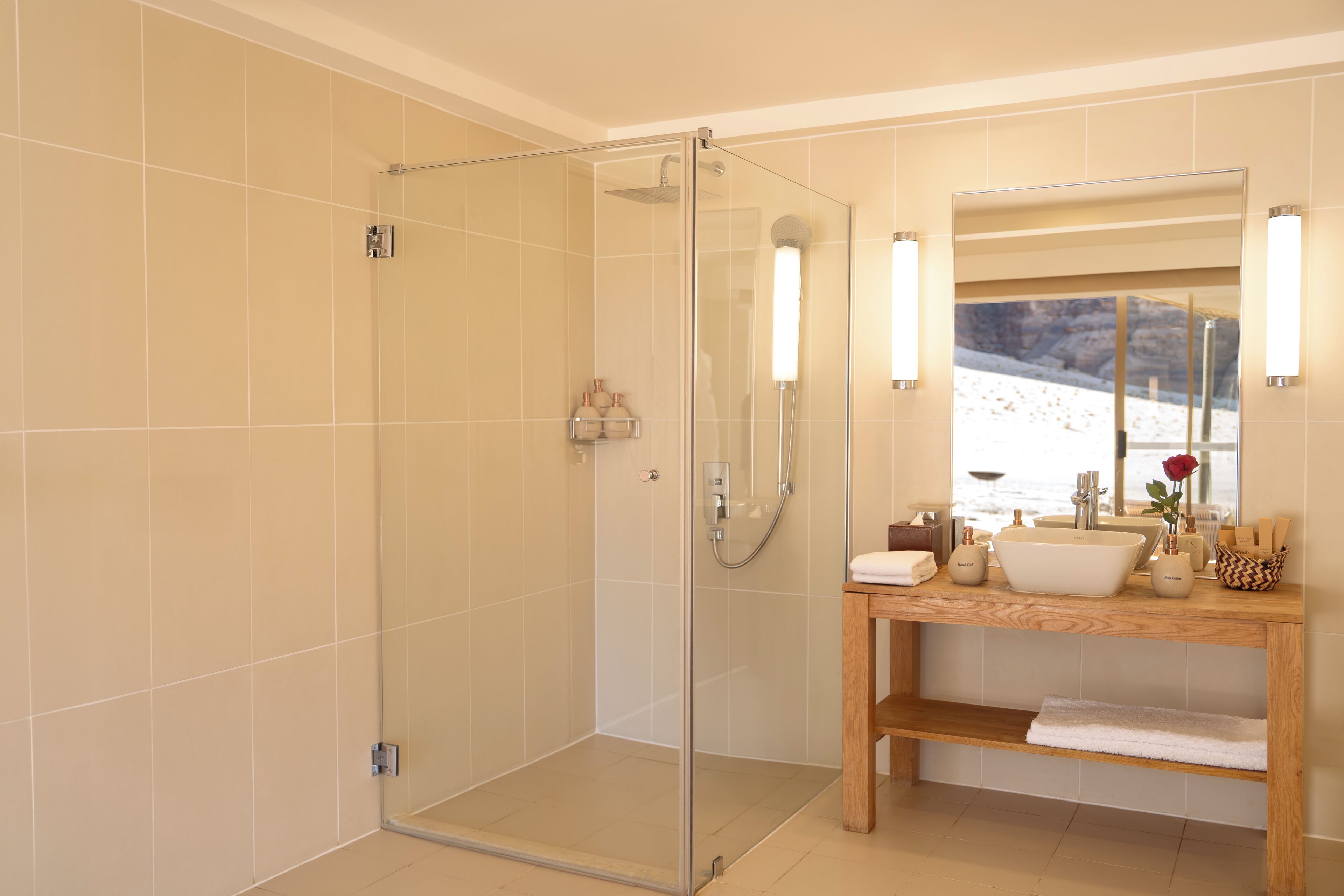 Ein modernes Badezimmer mit einer gläsernen Duschkabine, einem hölzernen Waschtisch und einem großen Spiegel sowie Blick auf eine verschneite Landschaft.