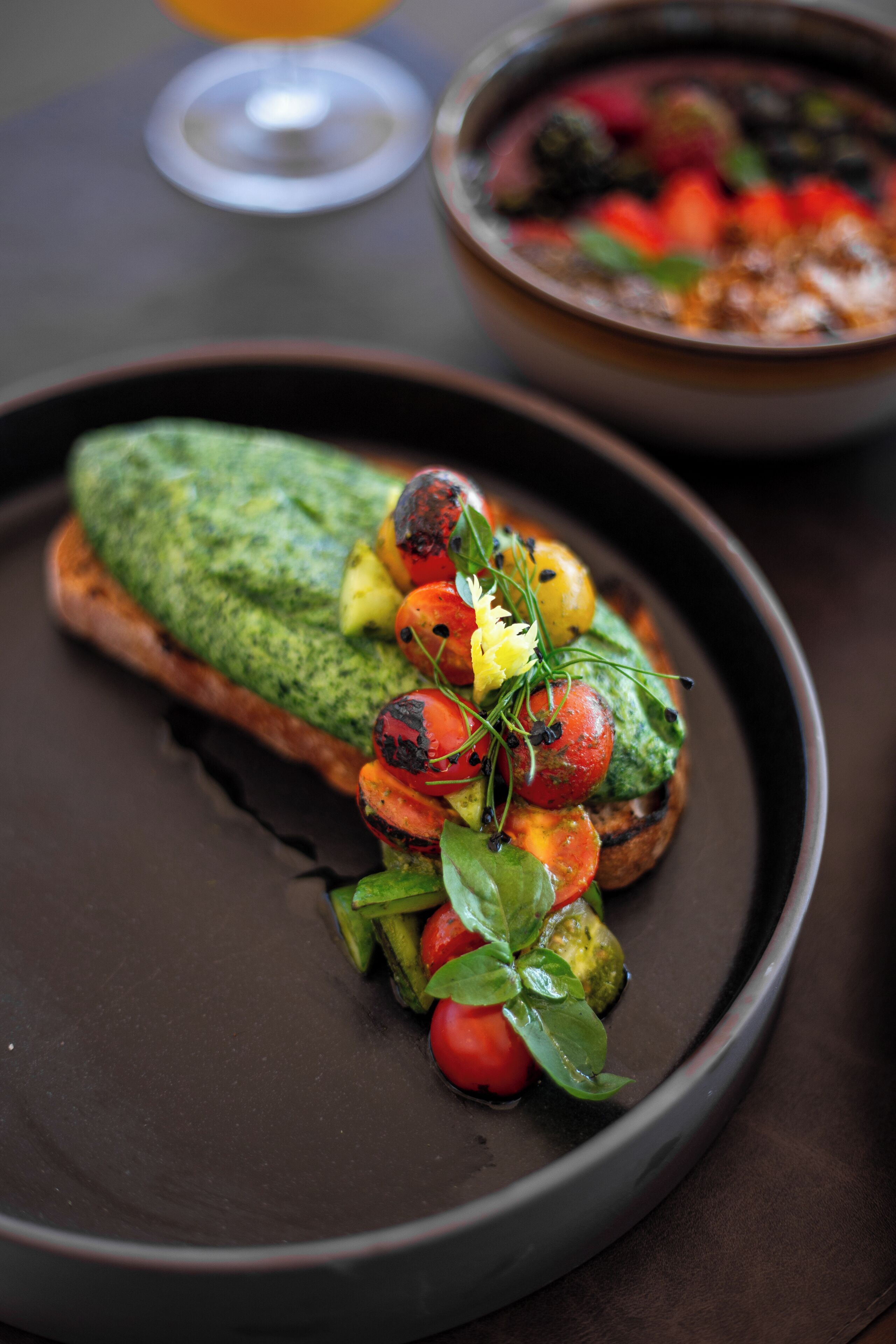 Ein Teller mit grüner Soße, vermutlich Pesto, und geröstetem Gemüse.