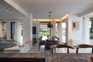 A modern living room with a dining area, large windows, and a view of the outdoors.