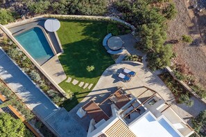An aerial view of a modern house with a swimming pool, a patio with lounge chairs, and a well-maintained lawn.