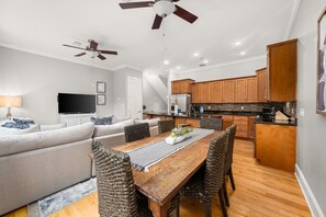 A modern living room with a sofa, dining table, and kitchen area with wooden cabinets and a built-in oven.