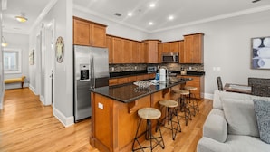 A modern kitchen with wooden cabinets, stainless steel appliances, and a central island with stools. - Coastal Daes | 4BR Townhome | Golf Cart Included | Santa Rosa Beach (Santa Rosa Beach)