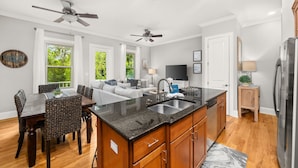 A modern kitchen with a central island, wooden cabinets, and a dining area with wicker chairs. - Coastal Daes | 4BR Townhome | Golf Cart Included | Santa Rosa Beach (Santa Rosa Beach)