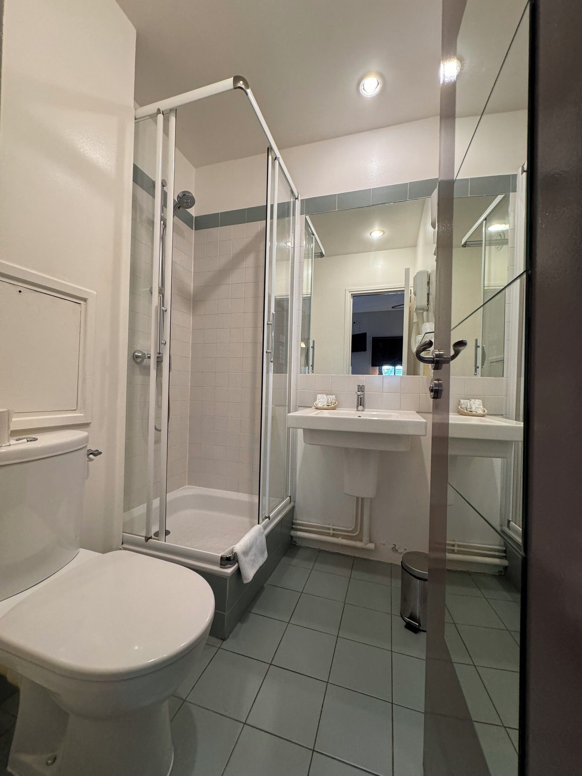 Un baño con ducha de mampara, inodoro, lavamanos y espejo.